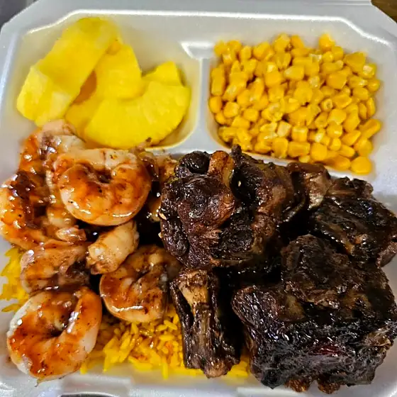 A loaded carnival plate piled with shrimp, oxtail and pineapple.